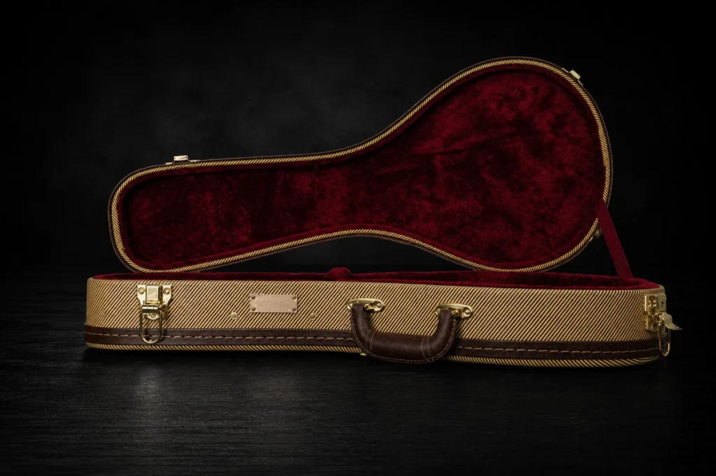 Nacho Bizness Custom vintage-style mandolin case open on a dark studio background, featuring a tweed exterior, burgundy plush interior, brass hardware, and brown leather handle.